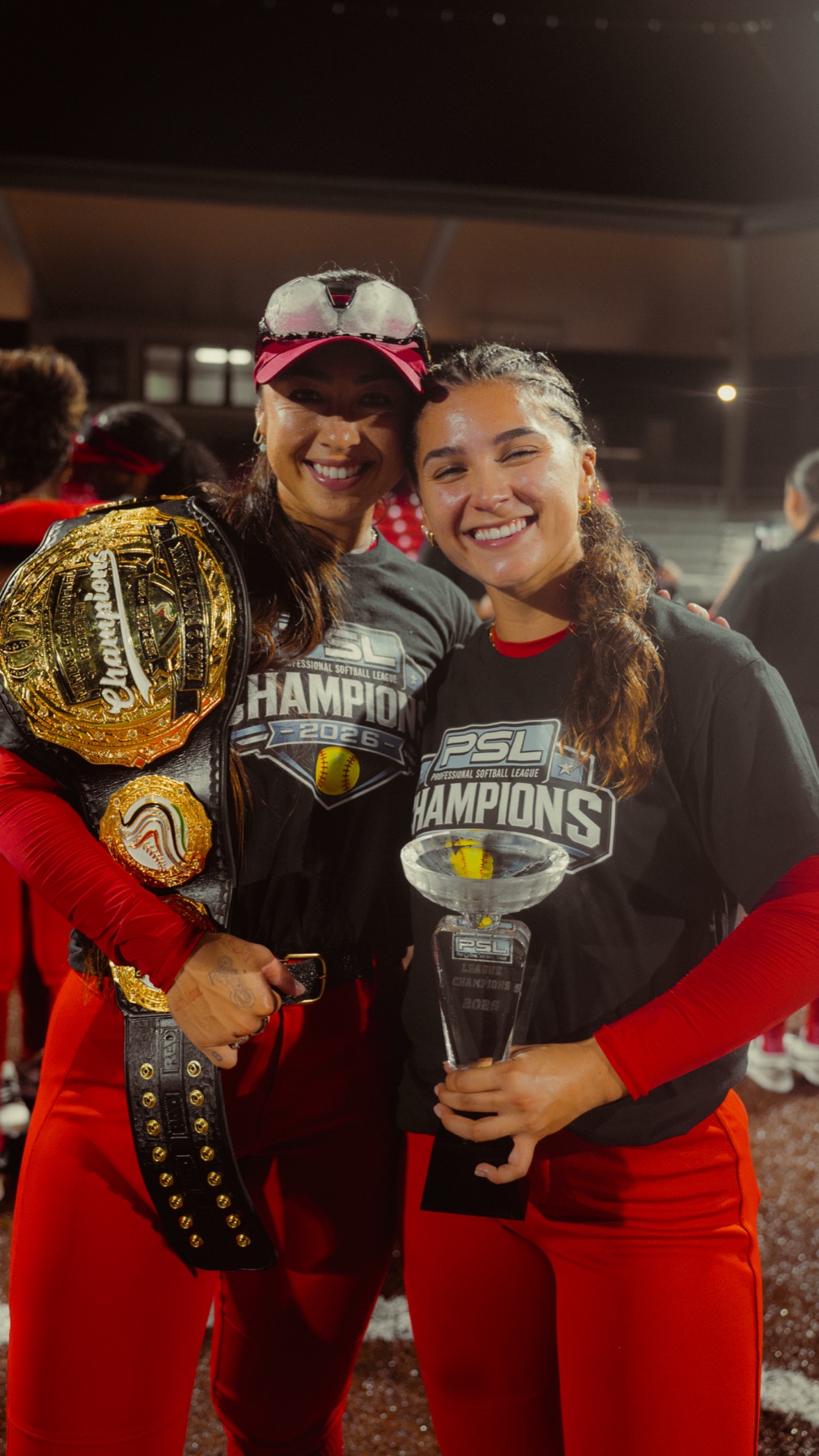 Two smiling players in PSL Champions shirts hold the championship belt and trophy
